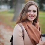 Portrait of a smiling woman holding a coffee cup in a serene autumn park setting.